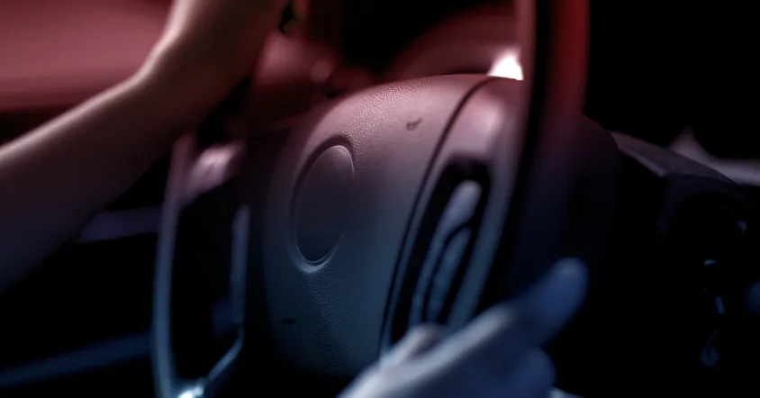 Close-up of a person’s hands on a steering wheel inside a dimly lit vehicle, symbolizing driving under the influence or intoxicated driving.