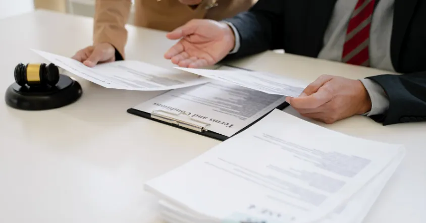 Two people review legal documents at a desk with a gavel nearby.